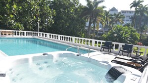 A hot tub with lounge chairs, surrounded by a white fence and palm trees. - Cozy Cottage, 5 minutes walk to beach, beautiful garden perfect relaxation spot (Ocho Rios)