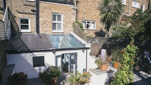 A small, private garden with a glass-roofed structure, potted plants, and a brick wall.