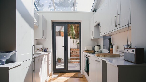 A modern kitchen with white cabinets, a black-framed door leading to a patio, and a skylight above.