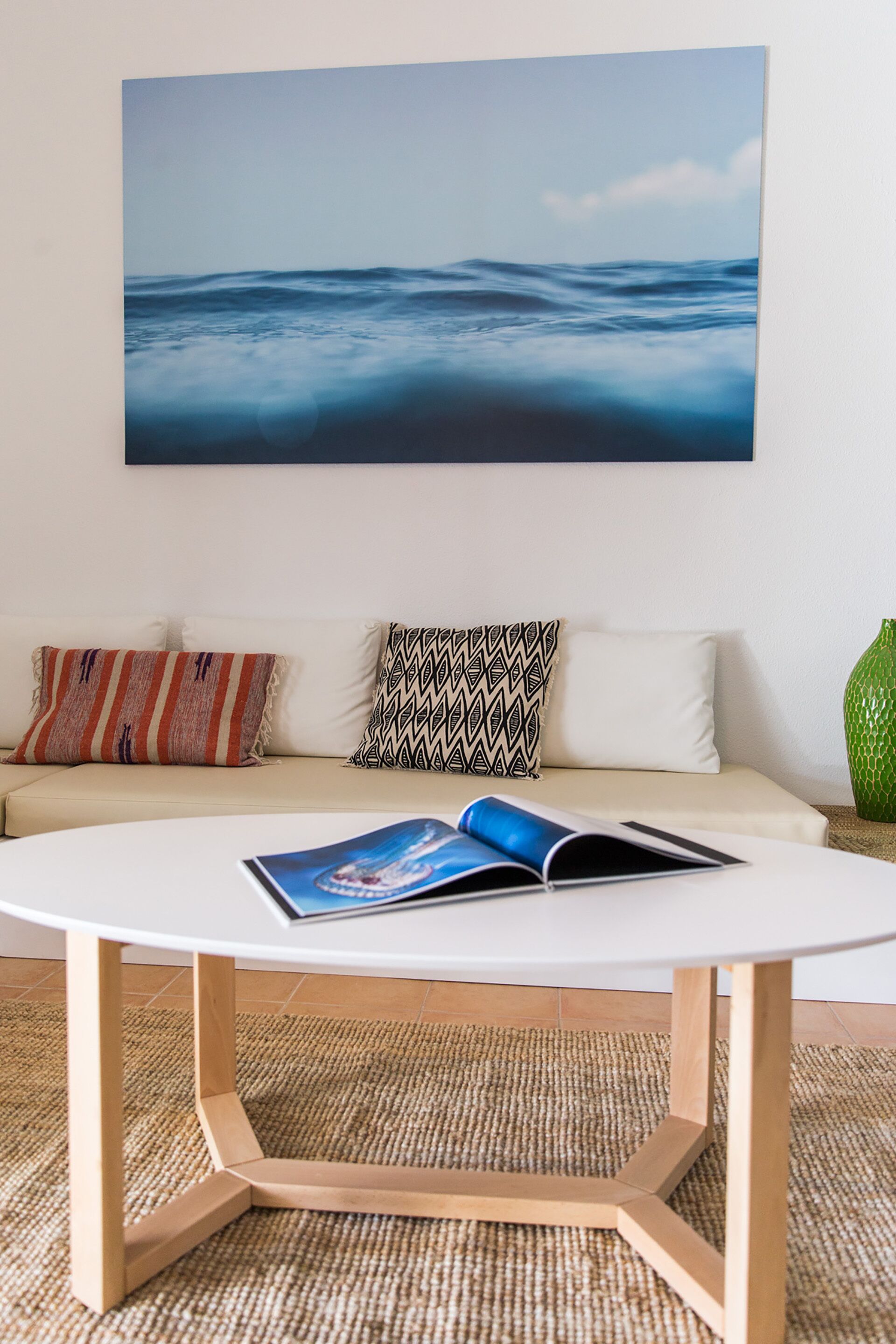 A living room with a round white coffee table, a beige sofa with patterned cushions, and a large abstract painting above the sofa.