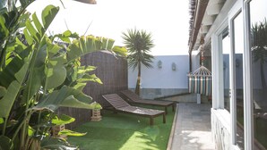A patio area with artificial grass, wooden lounge chairs, a palm tree, and a hanging hammock.