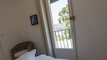 Un lit bien fait, avec du linge de lit blanc, dans une chambre donnant sur un balcon et une porte.