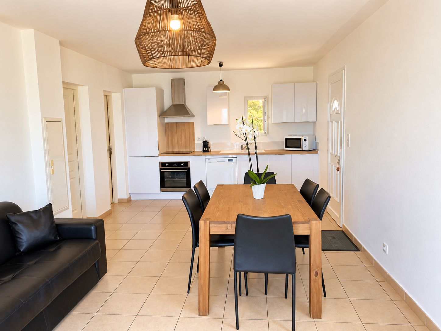 A modern kitchen with white cabinets, a wooden dining table, and black chairs.
