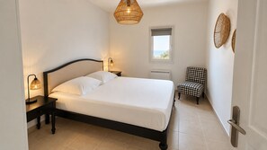 A bedroom with a bed, bedside lamps, a chair, a window, and a wall-mounted light fixture. - NEW APARTMENT WITH MAGNIFICENT VIEW OF SAINT FLORENT BAY (Saint-Florent)