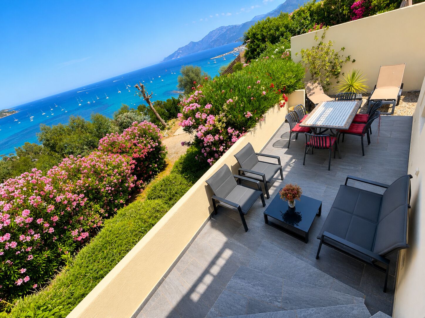 A terrace with outdoor seating, a view of the sea, and a mountain in the background.