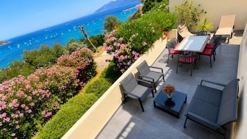 A terrace with outdoor seating, a view of the sea, and a mountain in the background.