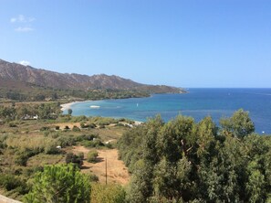 Un paysage côtier avec une plage, une mer d’un bleu limpide et des montagnes en arrière-plan.