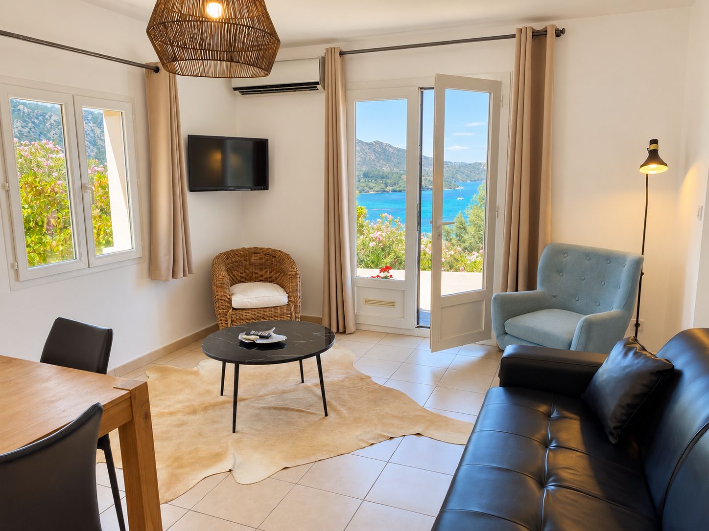 Un salon comprenant un canapé, un fauteuil, une table, un téléviseur et une vue sur la mer, accessible par une porte coulissante.