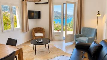 Un salon comprenant un canapé, un fauteuil, une table, un téléviseur et une vue sur la mer, accessible par une porte coulissante.