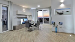 Un moderno salón con televisor, mesa de comedor, sillas y un amplio ventanal con vistas.
