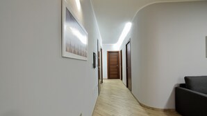 Un pasillo con suelo de madera, un sofá oscuro y una puerta de madera al final.