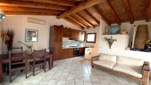 A cozy living area with a dining table, wooden chairs, a sofa, and a kitchen in the background.