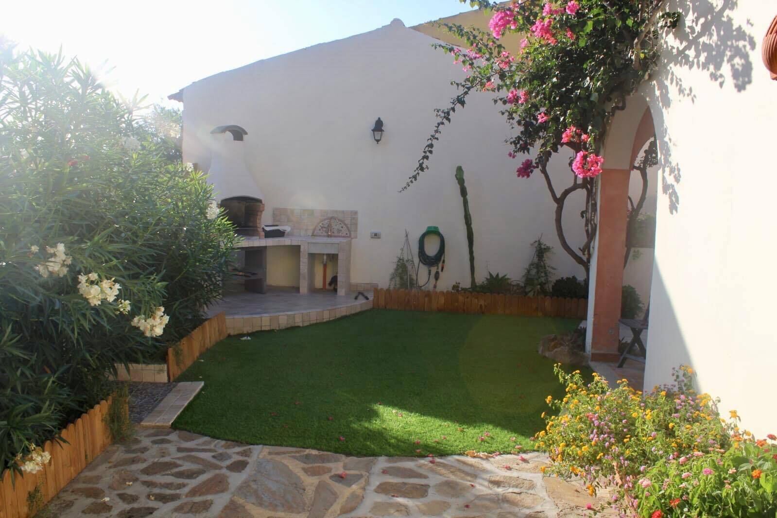 A courtyard with a well-maintained lawn, a stone pathway, and a white wall with a decorative arch.