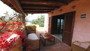 A covered outdoor seating area with wicker furniture, a table, and a view of the surrounding landscape.