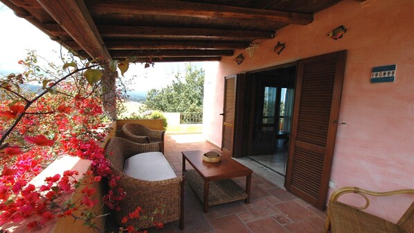 A covered outdoor seating area with wicker furniture, a table, and a view of the surrounding landscape.