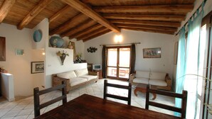 A cozy living room with a wooden ceiling, two sofas, a dining table, and a TV.