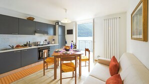 A modern kitchen with dark cabinets, a dining table, and chairs. There is a balcony with a view of the mountains. - Villa L'Approdo, Porlezza, Italy (Porlezza)