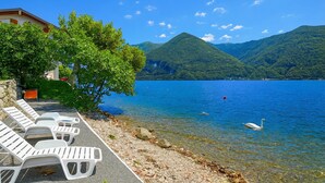 A lakeside view with a row of white lounge chairs, a building with a red roof, and mountains in the background. - Villa L'Approdo, Porlezza, Italy (Porlezza)