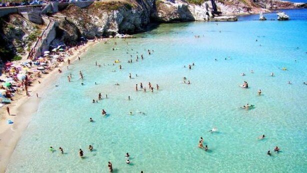 A beach with clear turquoise water, people swimming and sunbathing, and rocky cliffs in the background. - Bright, air-conditioned apartment with a large terrace a few steps from the sea (Terrasini)