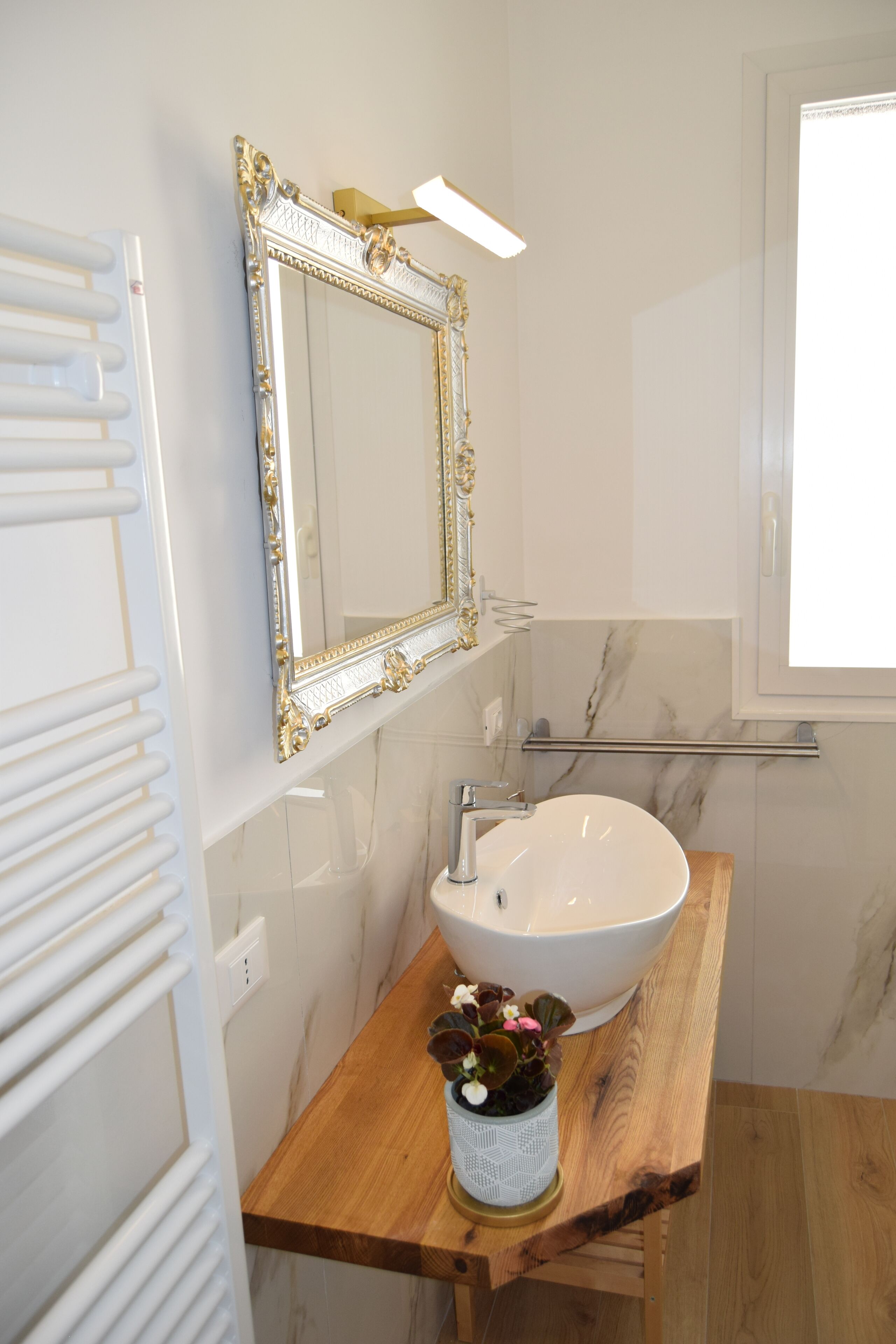 Ein Badezimmer mit einem weißen Waschbecken, einem spiegeln Spiegel mit goldener Rahmung und einer Holzkommode.