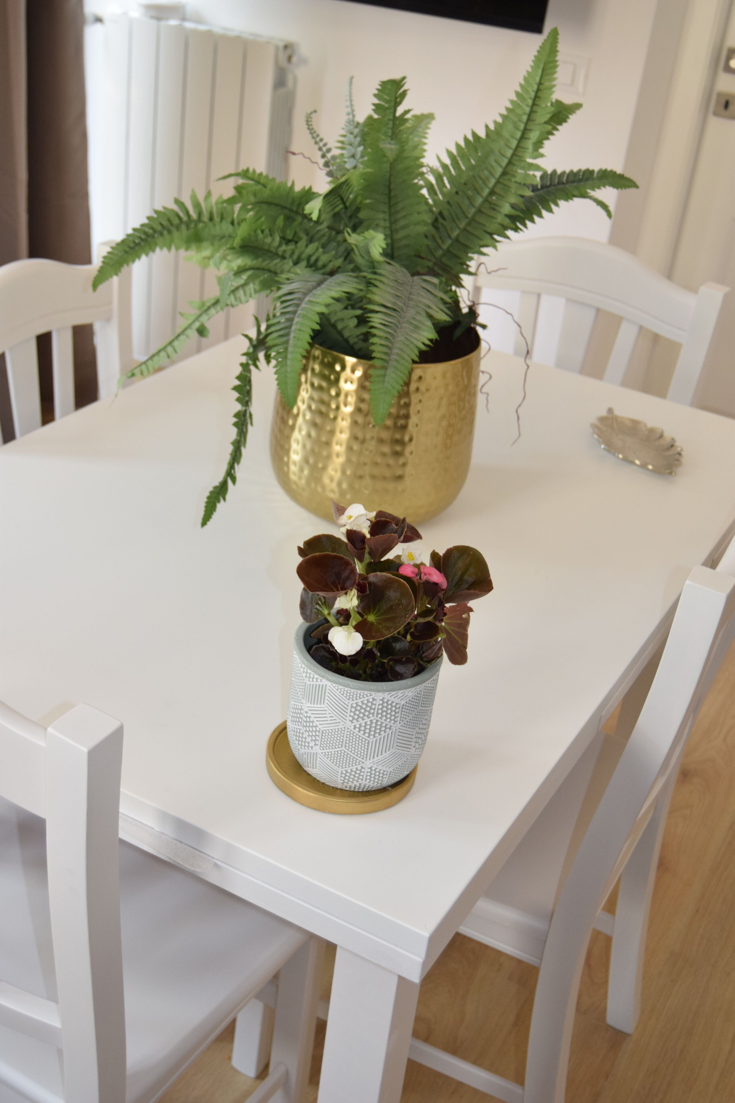 A white dining table with two potted plants, one in a gold pot and another in a patterned pot.