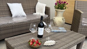 A wicker sofa with a white cushion, a wicker coffee table with a bottle of wine, two glasses, a bowl of strawberries, and a decorative plate. - Bright, air-conditioned apartment with a large terrace a few steps from the sea (Terrasini)