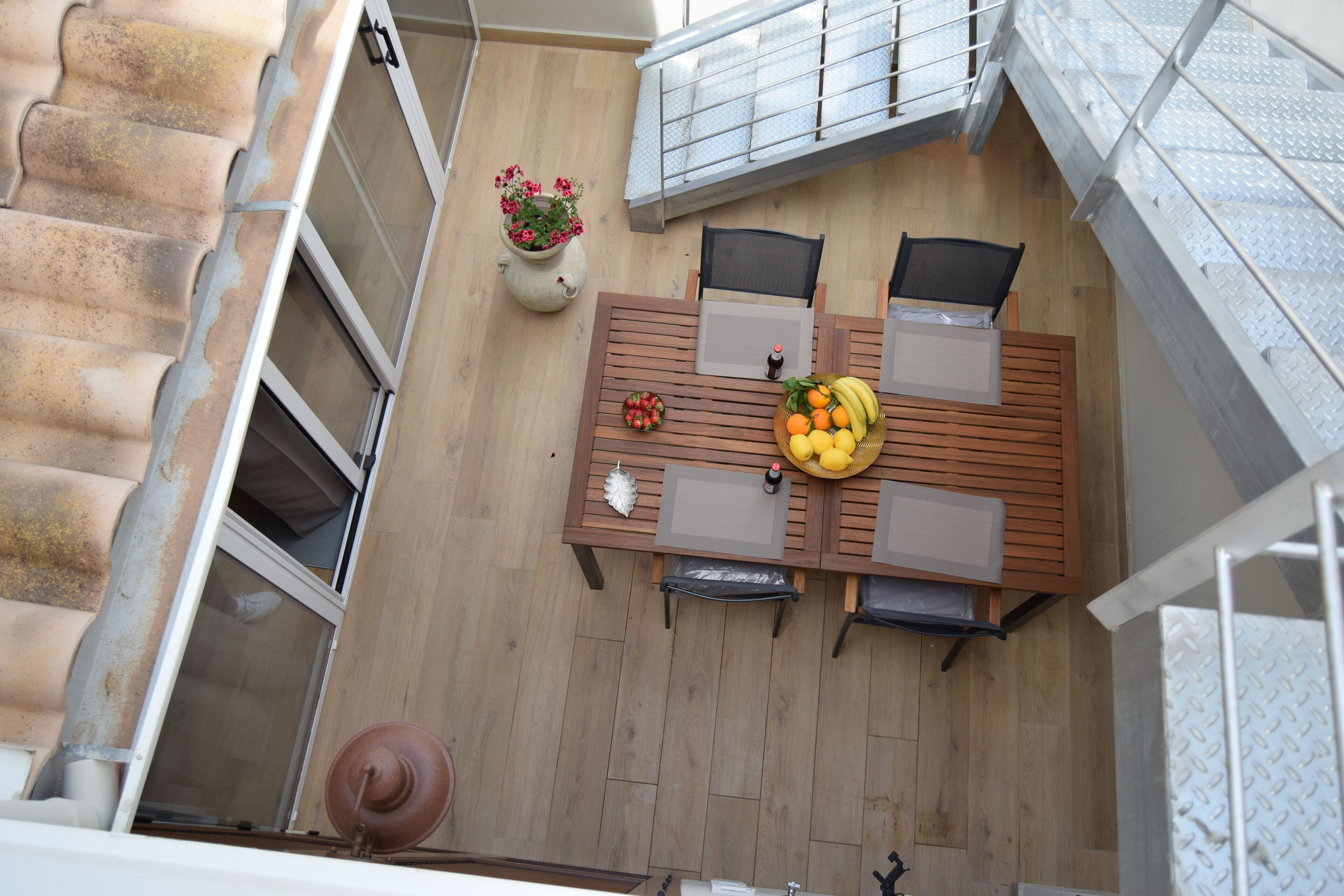 Una terraza de madera con una mesa, sillas, una planta en maceta y una escalera.