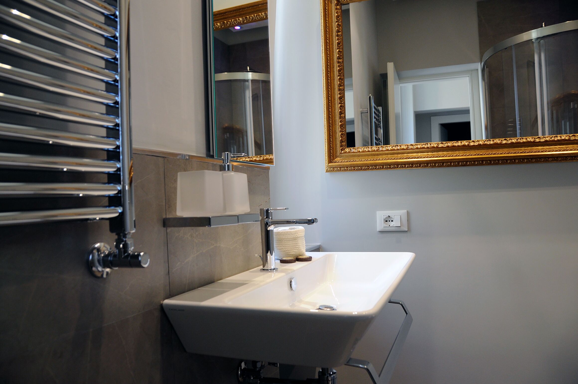 Une salle de bain moderne avec un lavabo blanc, des robinetteries chromées et un grand miroir doté d’un cadre doré.