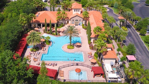 An aerial view of a resort with a large swimming pool, palm trees, and a building with a red roof.