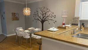 A modern kitchen with a granite countertop, stainless steel sink, and a dining area with white chairs.
