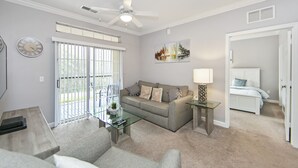 A living room with a sofa, a glass coffee table, a lamp, and a ceiling fan.