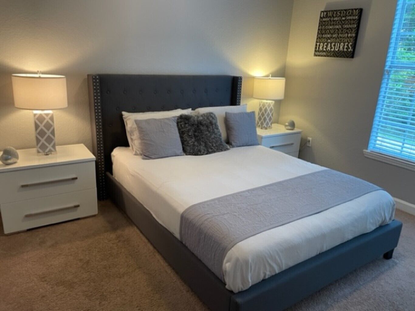 A bedroom with a large bed, two bedside tables, and a window with blinds.