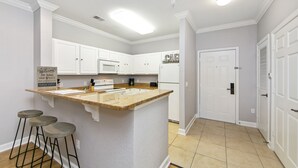 A kitchen with white cabinets, a granite countertop, and a built-in microwave. There are three stools and a sign on the countertop.
