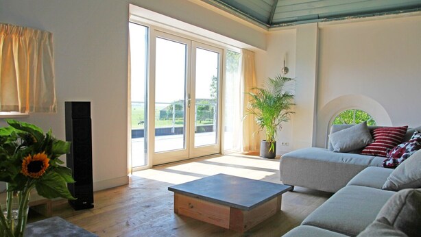 Una sala de estar moderna con un sofá gris, una mesa de centro de madera y un ventanal con vistas a un paisaje verde.