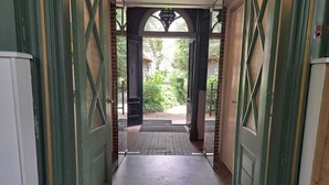 Un pasillo con puertas verdes, suelo de baldosas y vistas al exterior con vegetación.