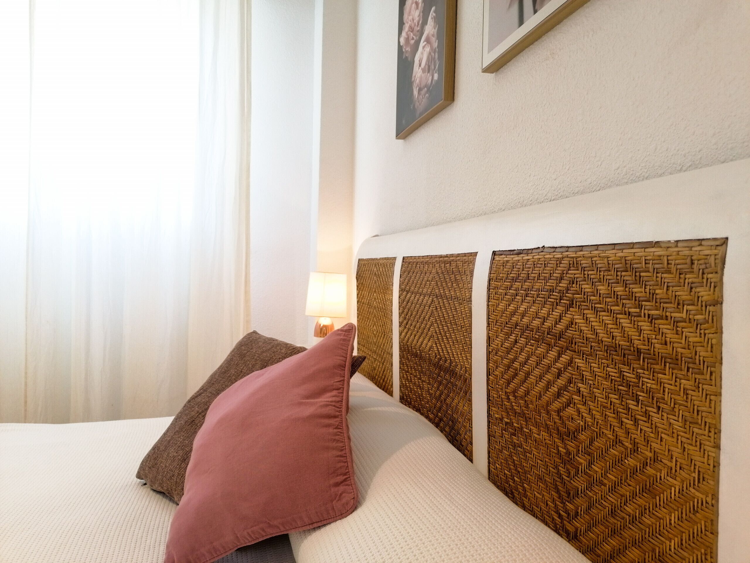 Ein Bett mit einem gewobenen Kopfteil, einem rosa Kissen und einem braunen Kissen.