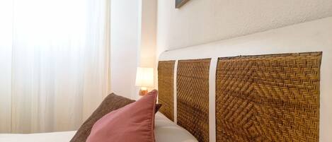 Ein Bett mit einem gewobenen Kopfteil, einem rosa Kissen und einem braunen Kissen.