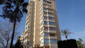 A multi-story building with balconies, surrounded by palm trees and other vegetation. - A78 EDIFICIO PEÑASOL 1º 3 (Calpe)