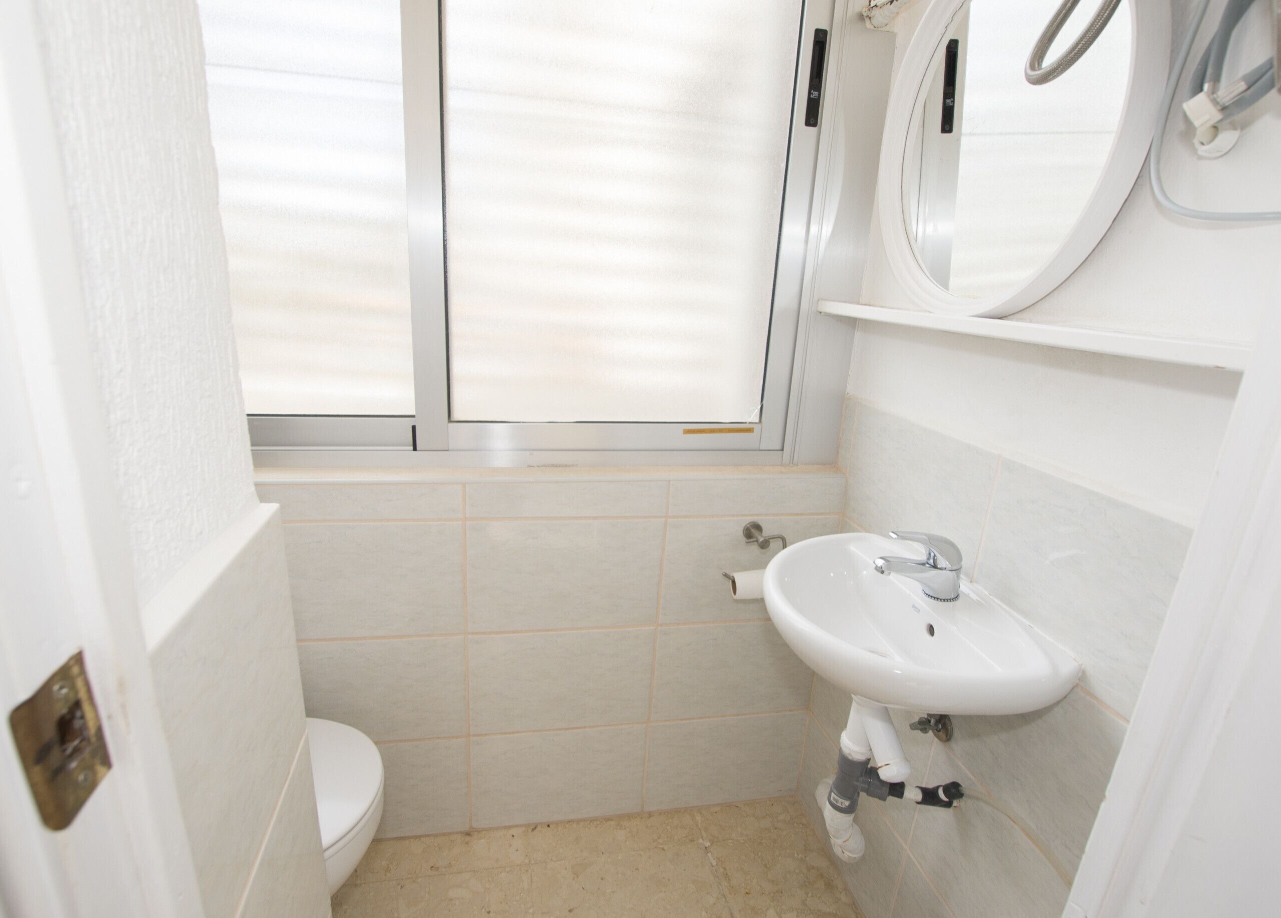 Un bagno piccolo e pulito, con il water, un lavandino e una finestra.