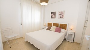 A neatly arranged bedroom with a large bed, a bedside table with a lamp, and a chair. - A78 EDIFICIO PEÑASOL 1º 3 (Calpe)
