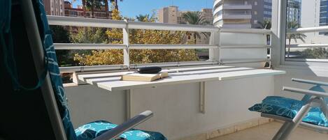 Un balcone con ringhiera bianca, una sedia blu e un tavolino con un libro e un telecomando.