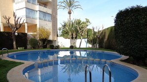 A swimming pool with a tiled edge, surrounded by grass and a hedge. - A78 EDIFICIO PEÑASOL 1º 3 (Calpe)