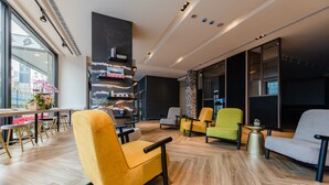 A modern interior with a wooden floor, yellow and grey chairs, a bookshelf, and large windows. - Wow-happy Hotel Taipei (Taipei)