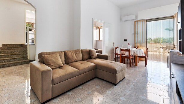 Een moderne woonkamer met een hoekbank, een eetgedeelte met een tafel en stoelen, en een trap naar een hoger niveau.