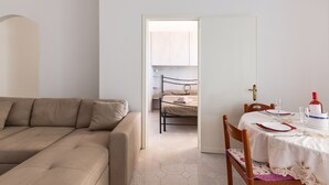 Een kamer met een beige bank, een eettafel gedekt met borden en glazen, en een bed met een wit hoofdeinde.