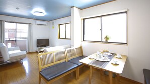 Una habitación con sofá, televisor, mesa de comedor con sillas y ventanas amplias.
