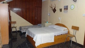 Une chambre à coucher comprenant un lit, deux chaises, une armoire, une horloge et un ventilateur fixé au mur.