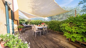 Eine Holzterrasse mit Tisch und Stühlen, umgeben von Grün und Blick auf Hügel.