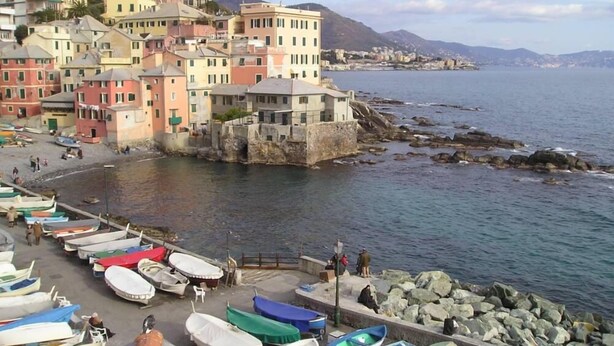 Une ville côtière aux bâtiments aux couleurs vives, avec un littoral rocheux et des bateaux amarrés le long de la jetée.