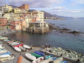 A coastal town with colorful buildings, a rocky shoreline, and boats docked along the pier.
